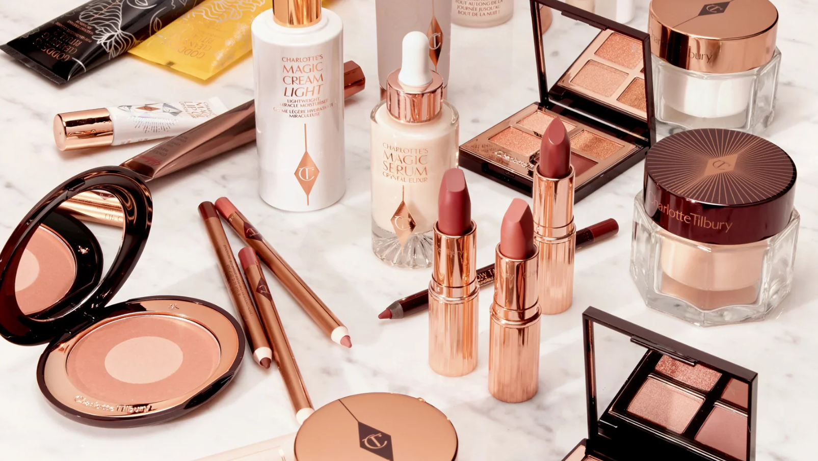 A variety of Charlotte Tilbury make-up products, including lipsticks, palettes, pencils, creams, and serum, arranged on a marble surface.